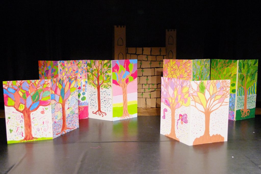 scène avec décors : panneaux avec arbres peints par des enfants, château en carton au fond