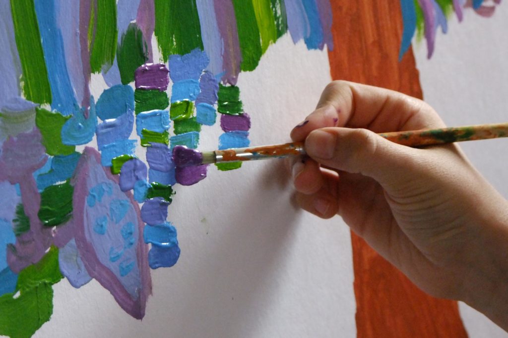 gros plan : main tenant un pinceau, peignant de petites touches de couleurs, bleu, vert et violet