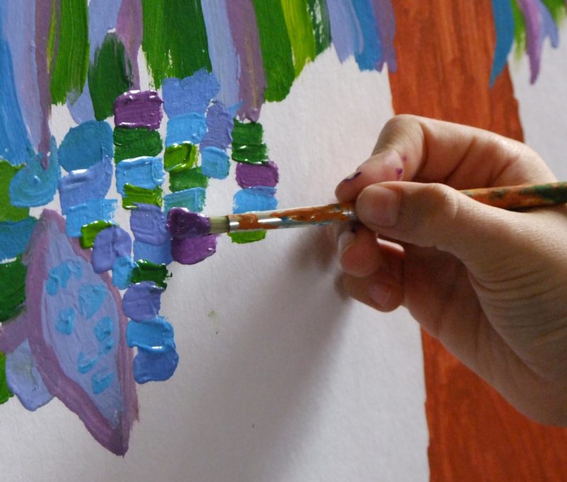 gros plan : main tenant un pinceau, peignant de petites touches de couleurs, bleu, vert et violet
