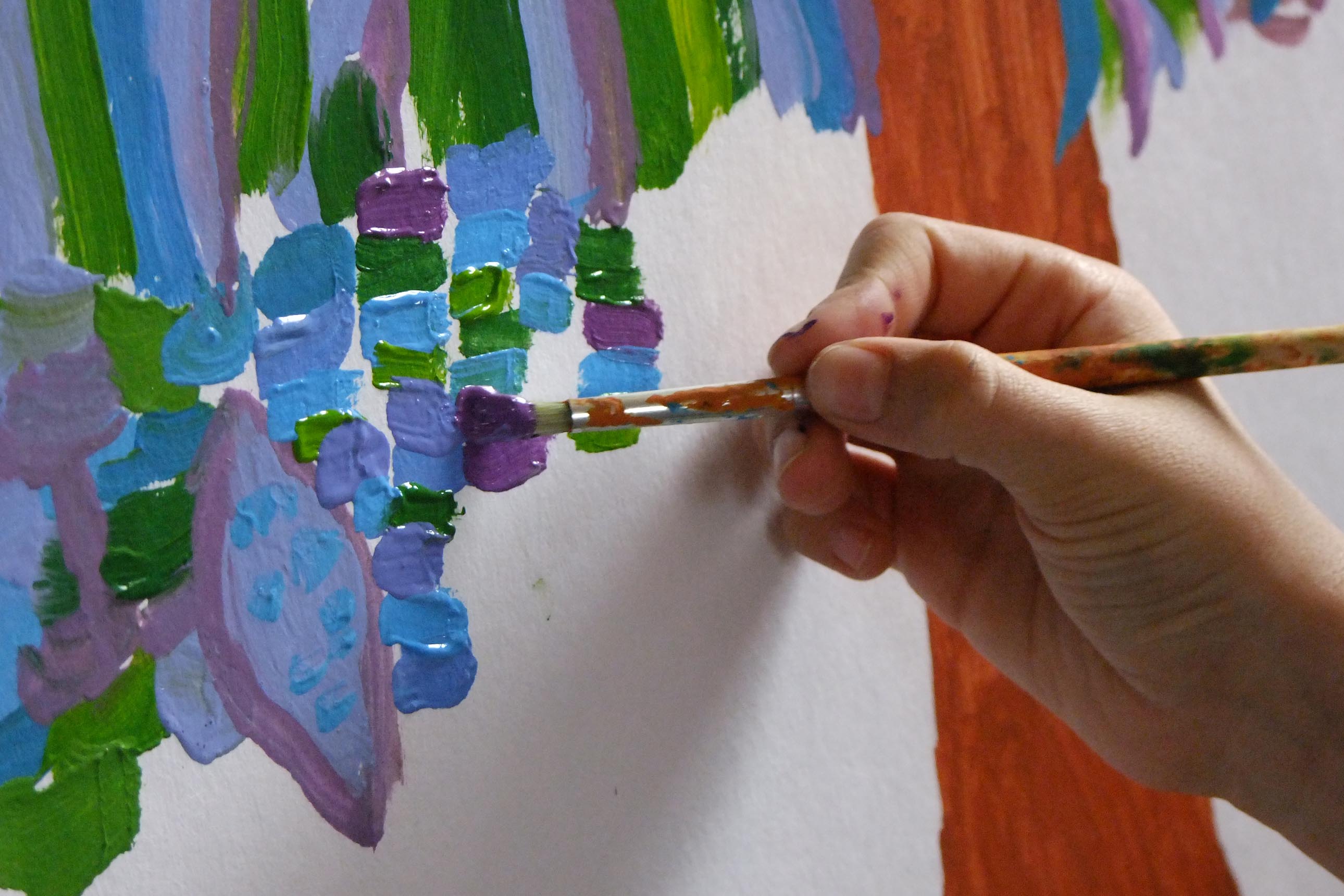 gros plan : main tenant un pinceau, peignant de petites touches de couleurs, bleu, vert et violet