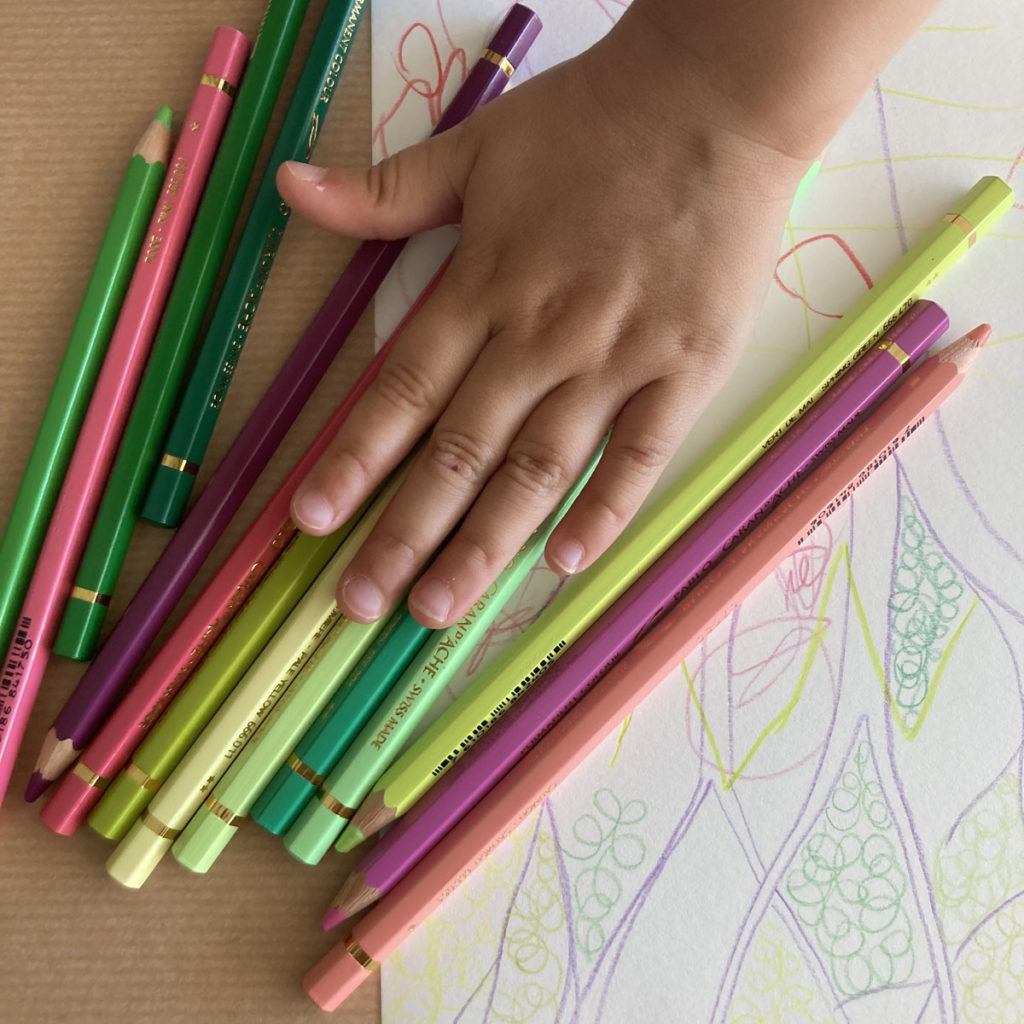 gros plan sur une main d'enfant, des crayons de couleur et un dessin