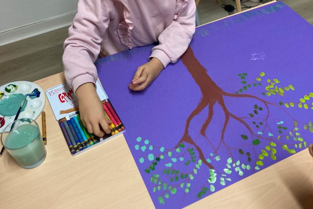 photo montrant des mains d'enfant avec un dessin grand format d'un arbre sur fond violet