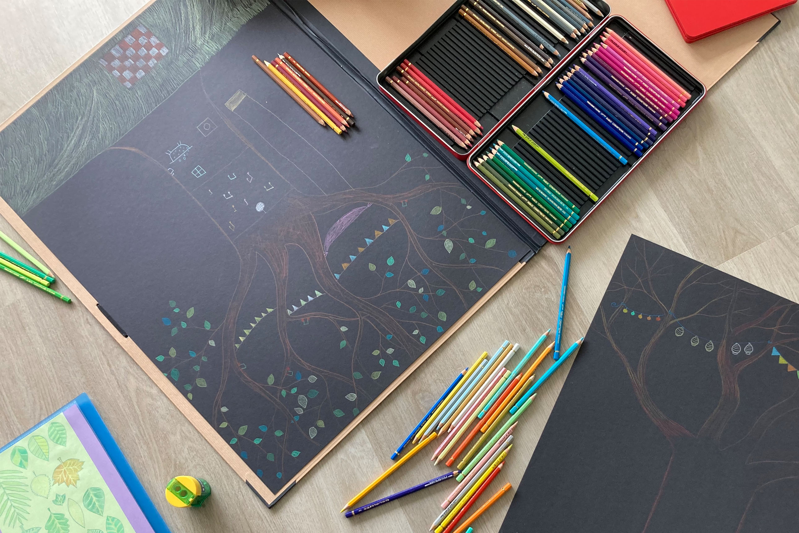grand dessin d'arbre aux crayons de couleur, sur fond noir, et boîte de crayons