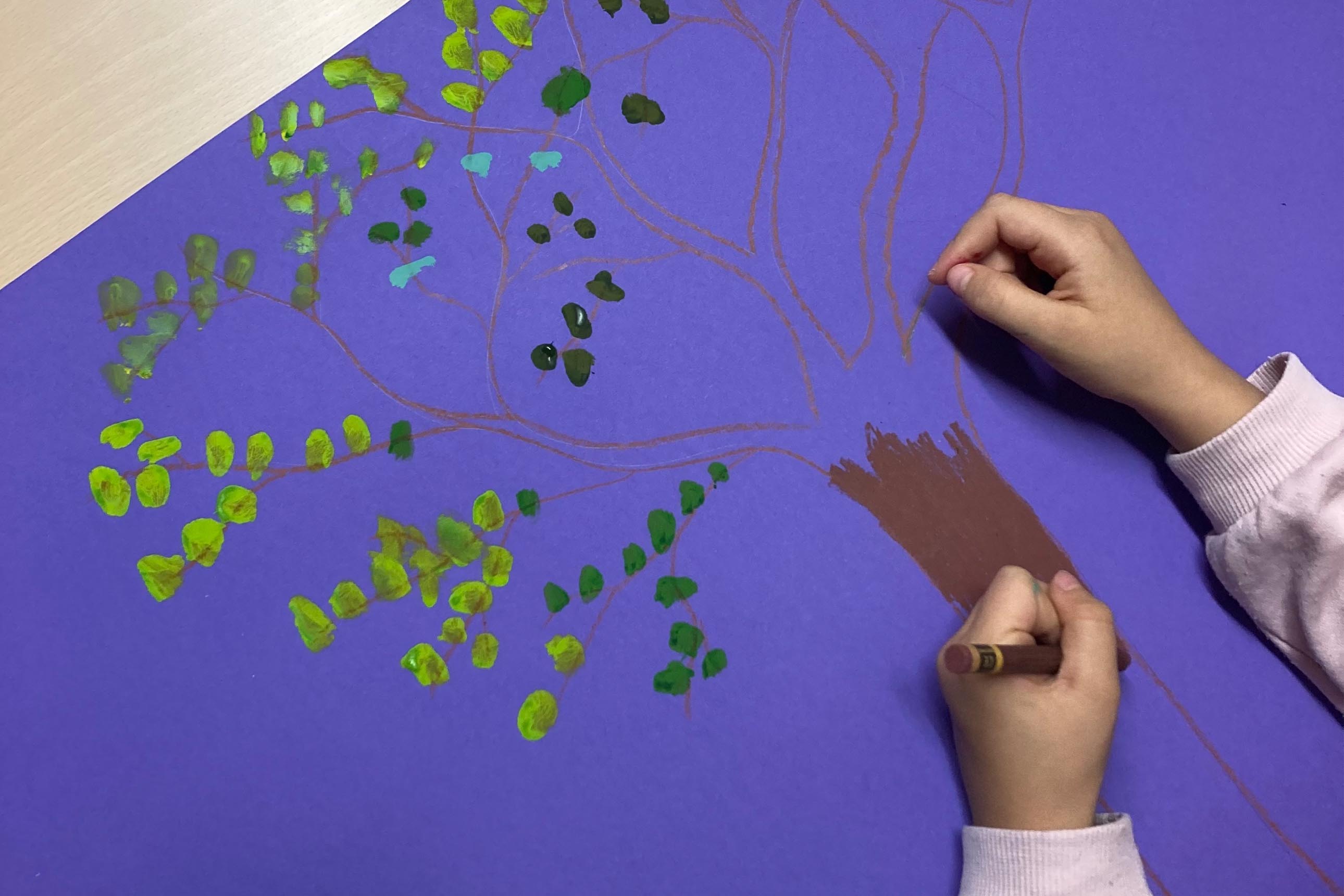 gros plan sur mains d'enfant dessinant un arbre aux pastels et peinture sur fond violet