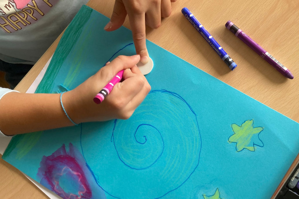 gros plan sur les mains d'enfant en train de dessiner une spirale et des étoiles sur une feuille bleue