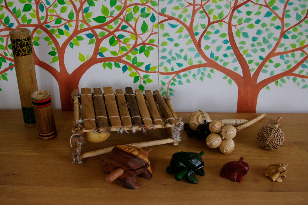 balafon, des guiros-grenouilles, maracasses, bâton de pluie devant un dessin d'arbre