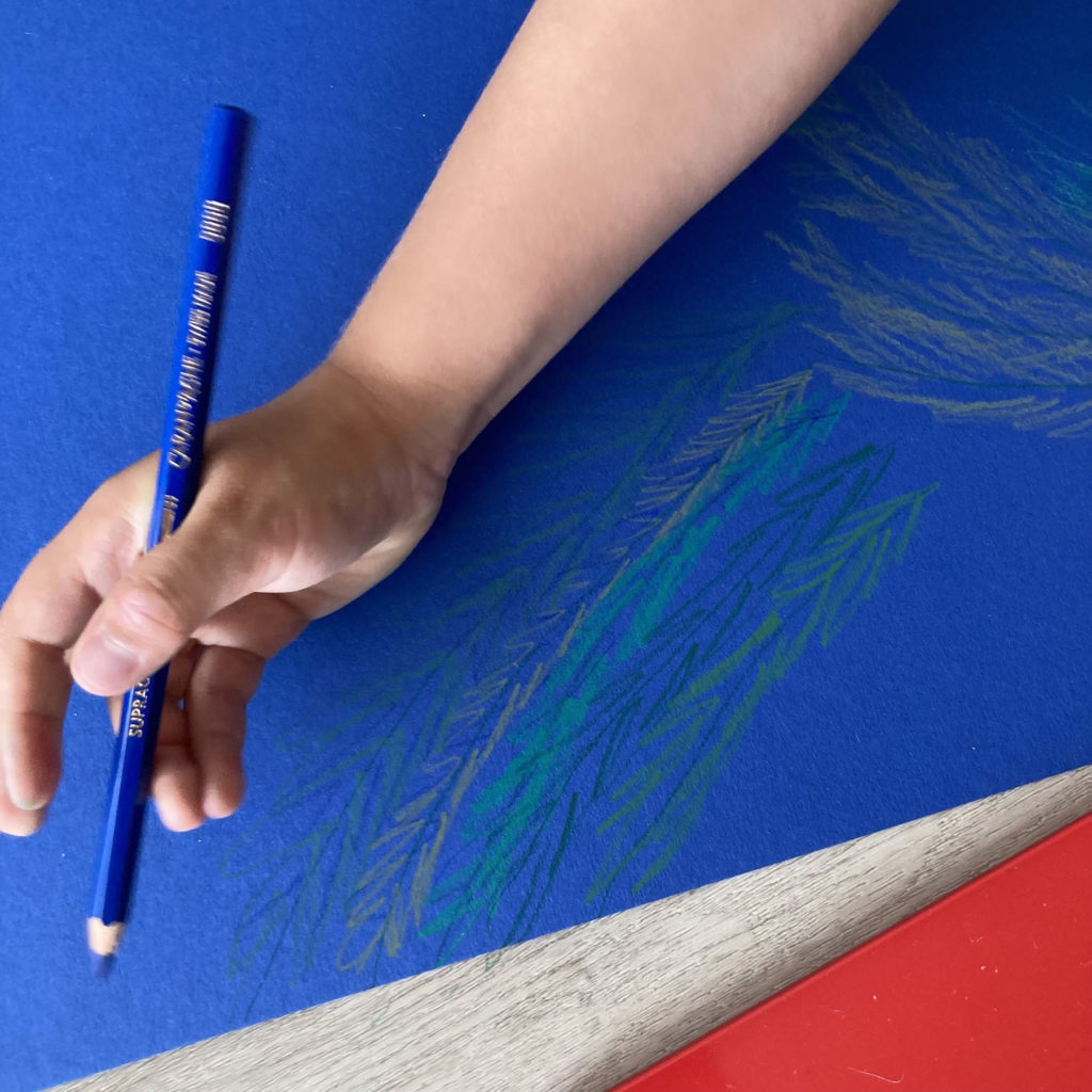gros plan, main d'enfant dessinant des feuillages sur une grande feuille bleue