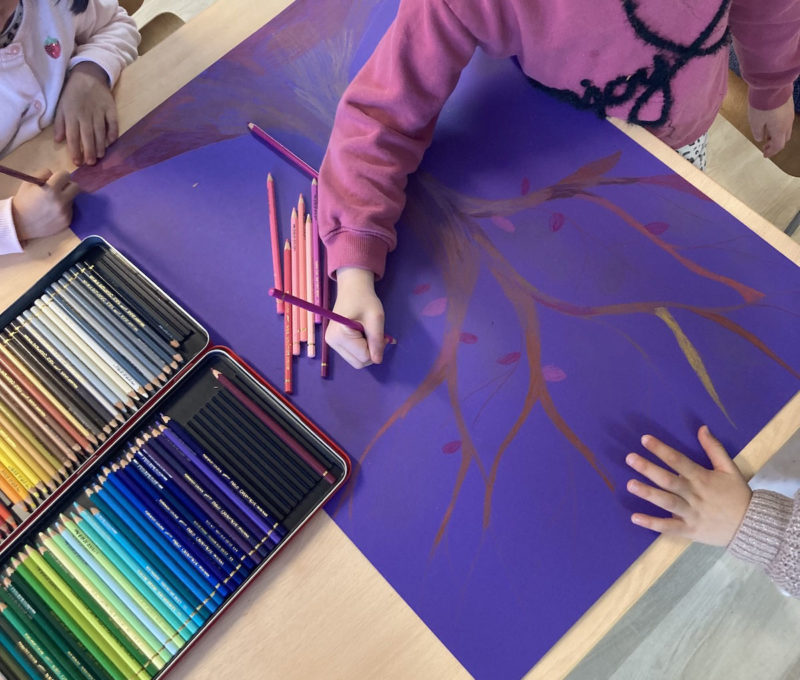 Gos plan sur un dessin d'arbre sur fond violet, 3 enfants dessinent sur le même dessin