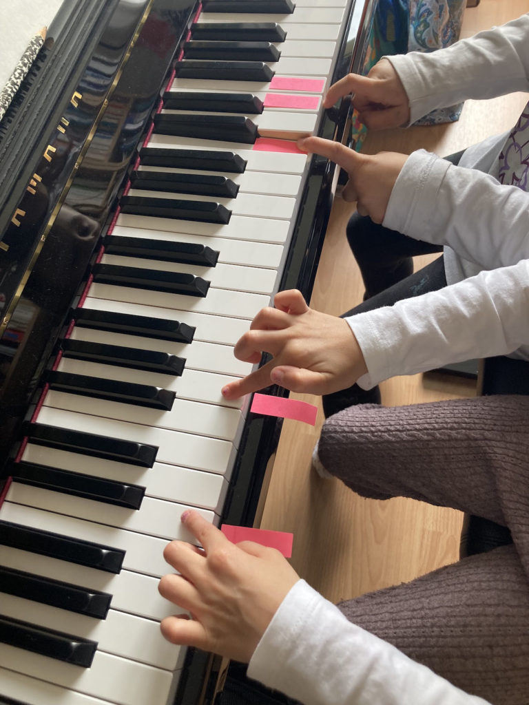 gros plan sur des mains d'enfant jouant du piano, des post-it sont collés sur certaines touches