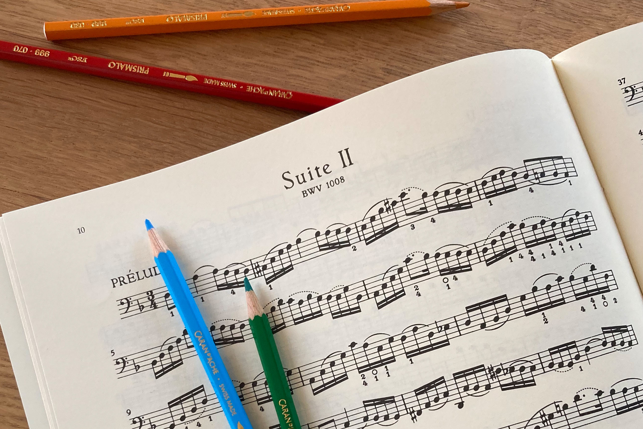 gros plan sur une partition "suite II" (suite pour violoncelle de Bach), quelques crayons de couleur sont posés sur la partition
