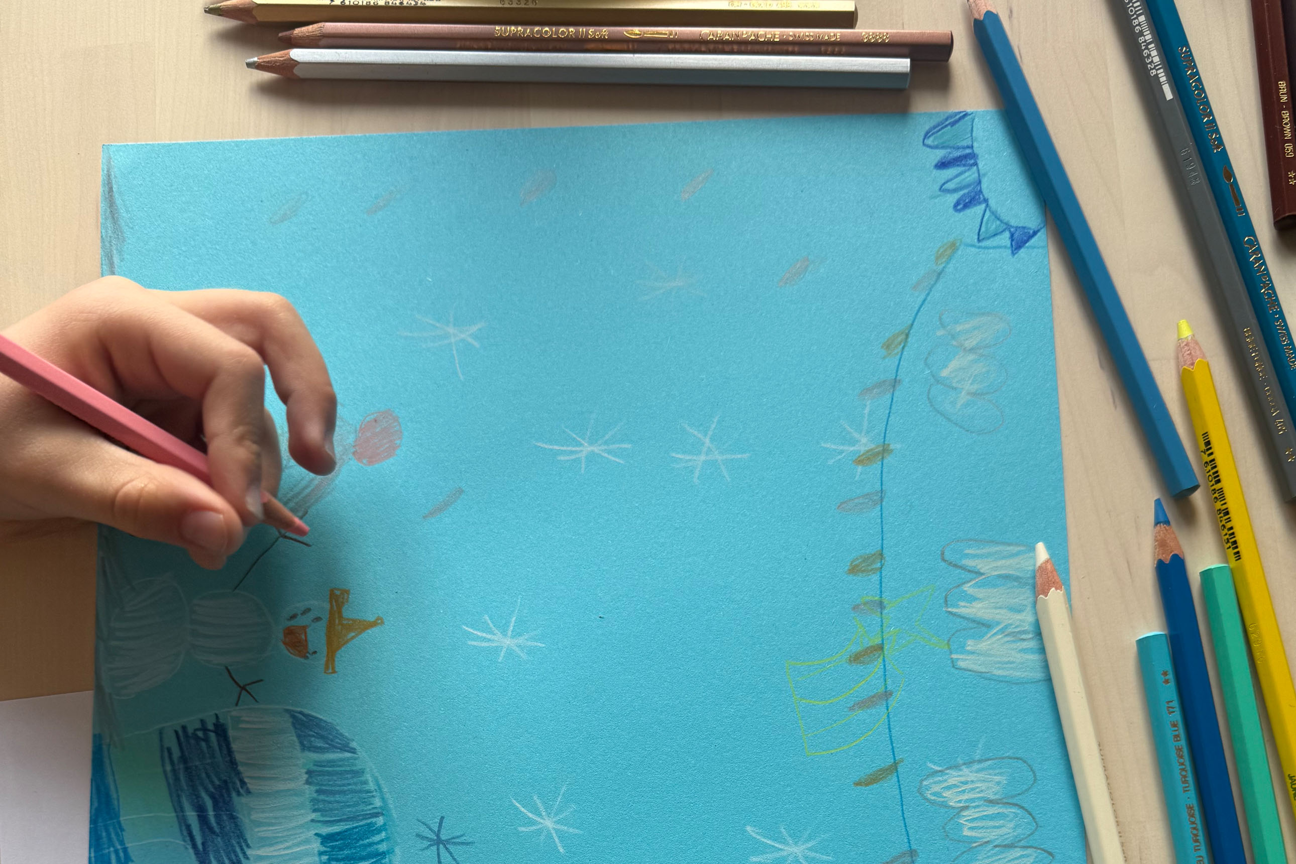 gros plan sur la main et le dessin d'un enfant : igloo, bonhomme de neige, paysage hivernal