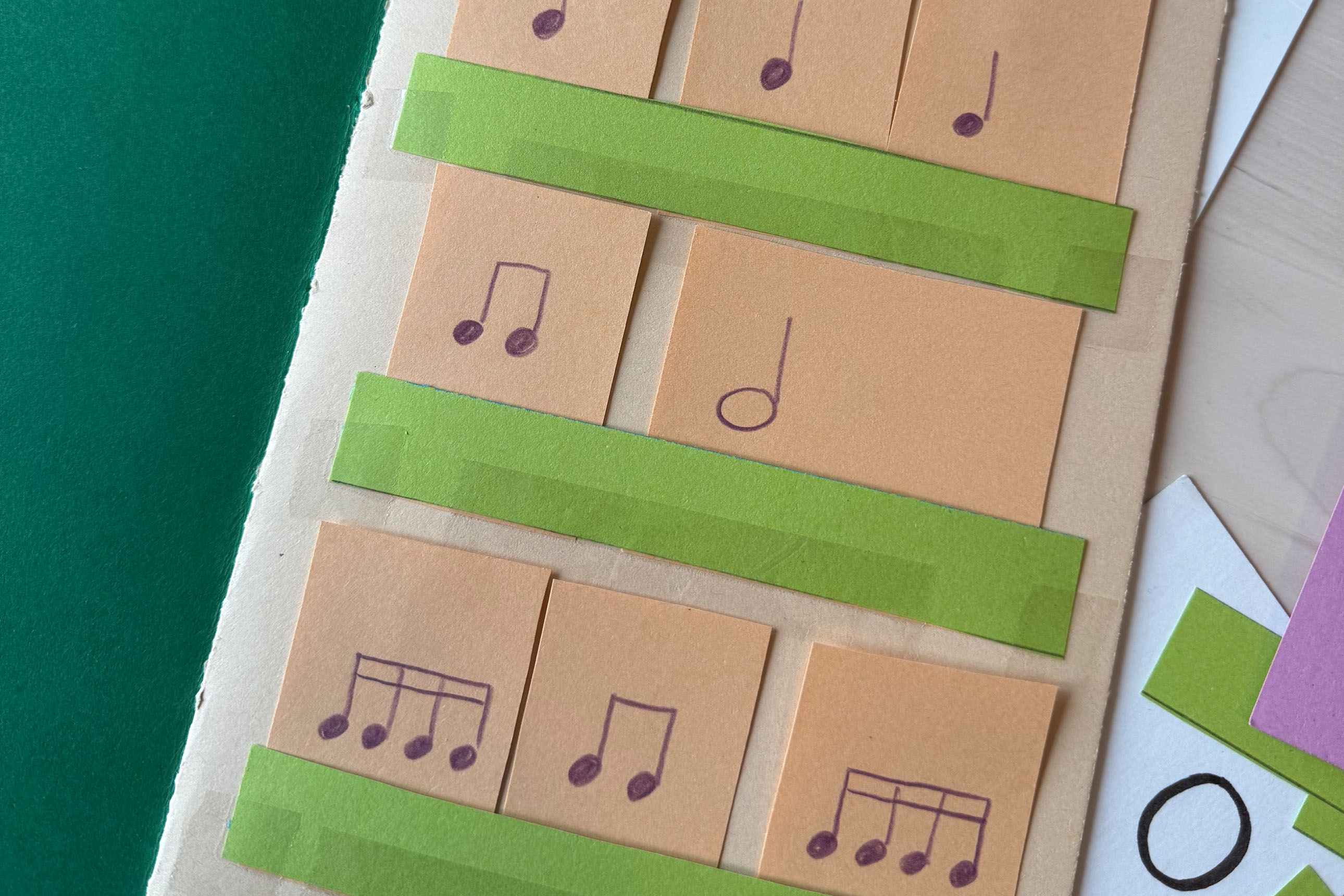 gros plan sur un cahier d'initiation musicale : petites cartes avec différents rythmes, se plaçant sur des "étagères" scotchées sur la page, de sorte que l'enfant peut changer l'ordre des cartes