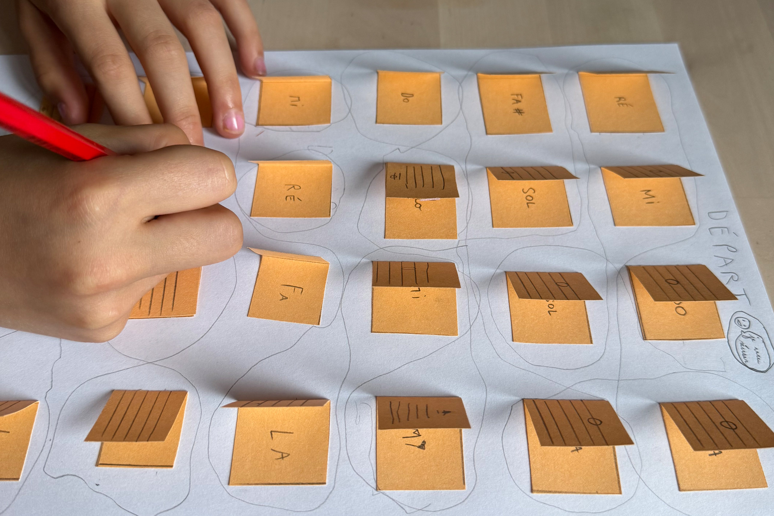 gros plan sur une partition-jeu avec des languettes pour deviner les notes de musique, mains de l'enfant en train de dessiner